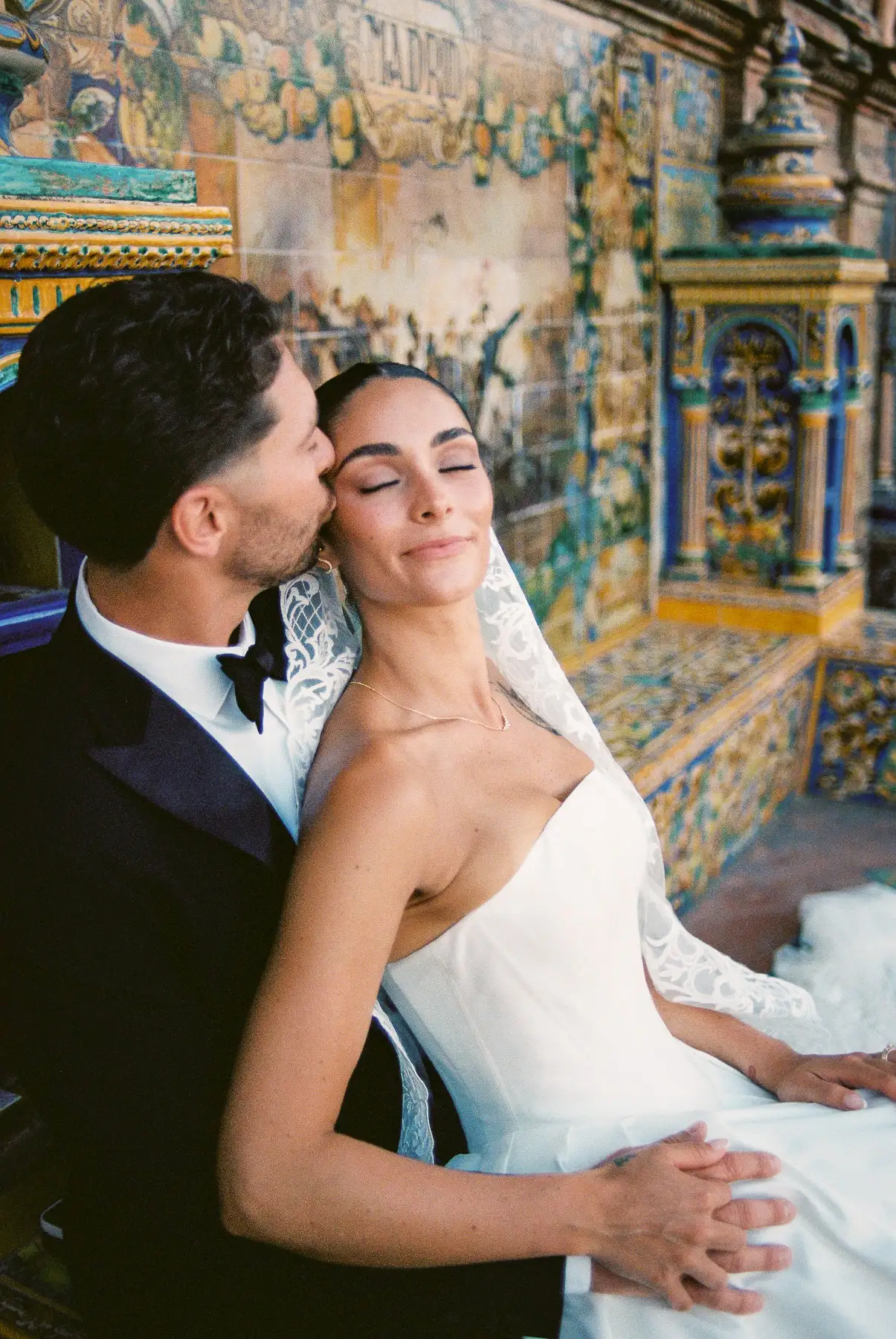 Pareja en la Plaza de España de Sevilla; él la besa en la sien mientras ella cierra los ojos, fotografiado en película